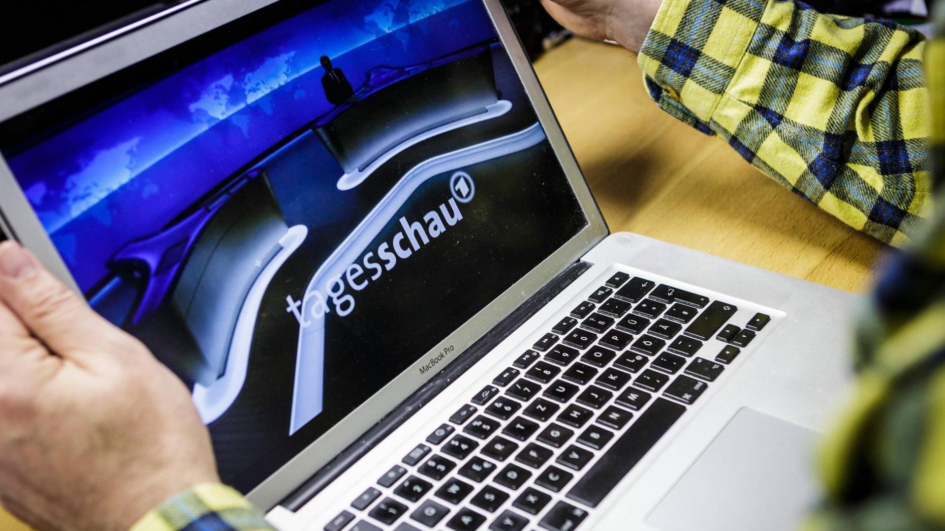 Mensch sitzt am Tisch mit einem Laptop, auf dessen Display das Tagesschau-Studio und -Logo zu sehen ist. Mensch sitzt am Tisch mit einem Laptop, auf dessen Display das Tagesschau-Studio und -Logo zu sehen ist.