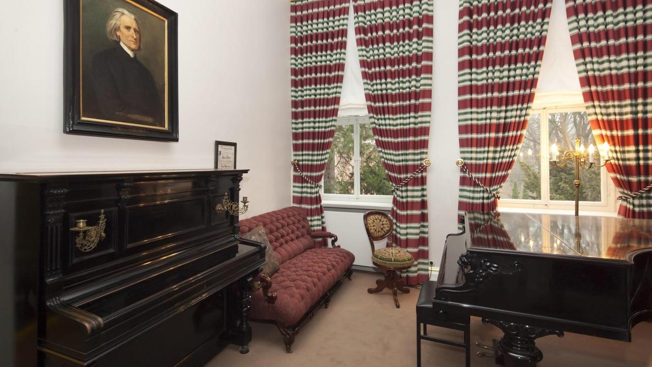 Blick in den Musiksalon im Liszt-Haus in Weimar mit Flügel, Klavier und markanten, bunt gestreiften Fenstervorhängen. Blick in den Musiksalon im Liszt-Haus in Weimar mit Flügel, Klavier und markanten, bunt gestreiften Fenstervorhängen.