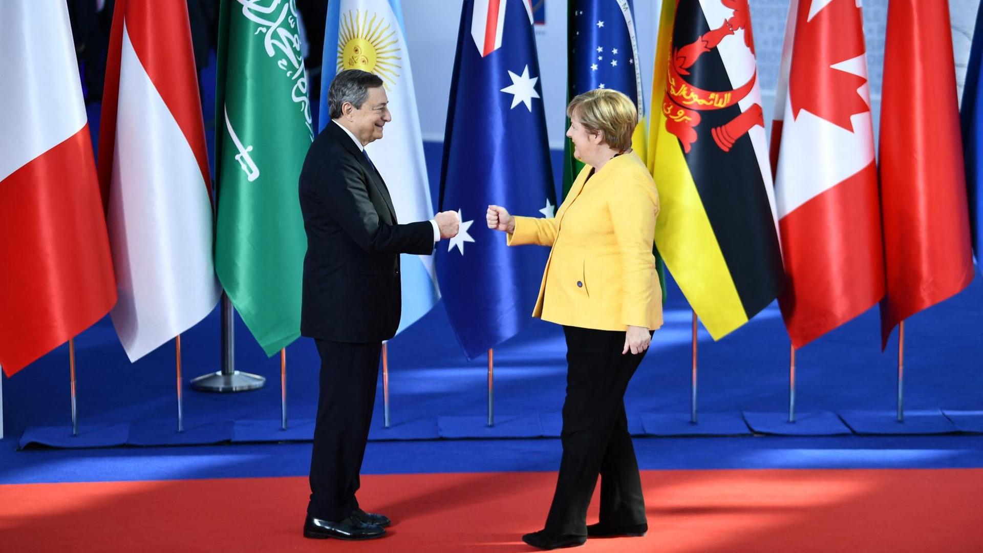 Draghi und Merkel geben sich die Hand. Hinter ihnen stehen die Fahnen von den G-20-Ländern. Draghi und Merkel geben sich die Hand. Hinter ihnen stehen die Fahnen von den G-20-Ländern.