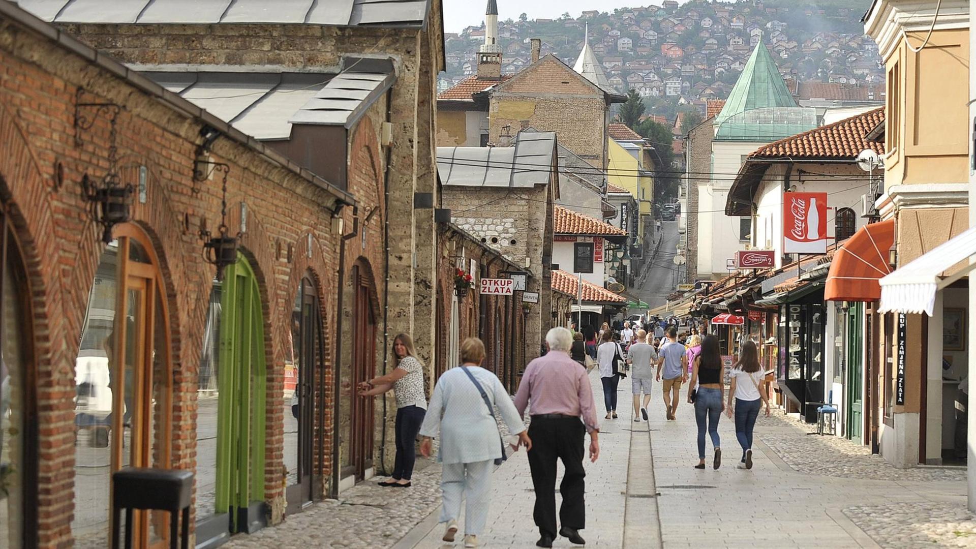 Eine Fußgänger-Straße in der Altstadt Sarajevos mit Blick auf die bewohnten Hügel im Hintergrund. Links ein altes Backsteingebäude mit Torbögen. Aufgenommen am 22.06.2016 Eine Fußgänger-Straße in der Altstadt Sarajevos mit Blick auf die bewohnten Hügel im Hintergrund. Links ein altes Backsteingebäude mit Torbögen. Aufgenommen am 22.06.2016