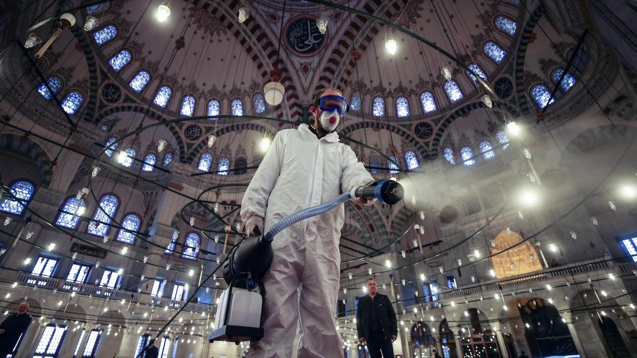 Ein Arbeiter in Schutzkleidung und mit Mundschutz desinfiziert die historische Fatih-Moschee in Istanbul.