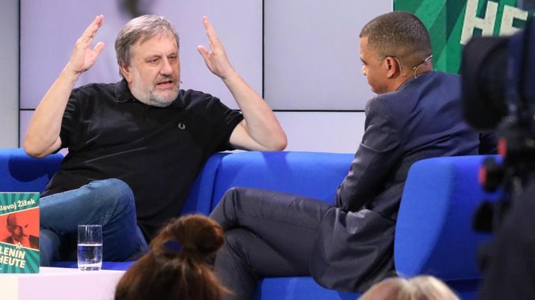 Slavoj Žižek sitzt auf einem Sofa und gestikuliert wild Slavoj Žižek sitzt auf einem Sofa und gestikuliert wild