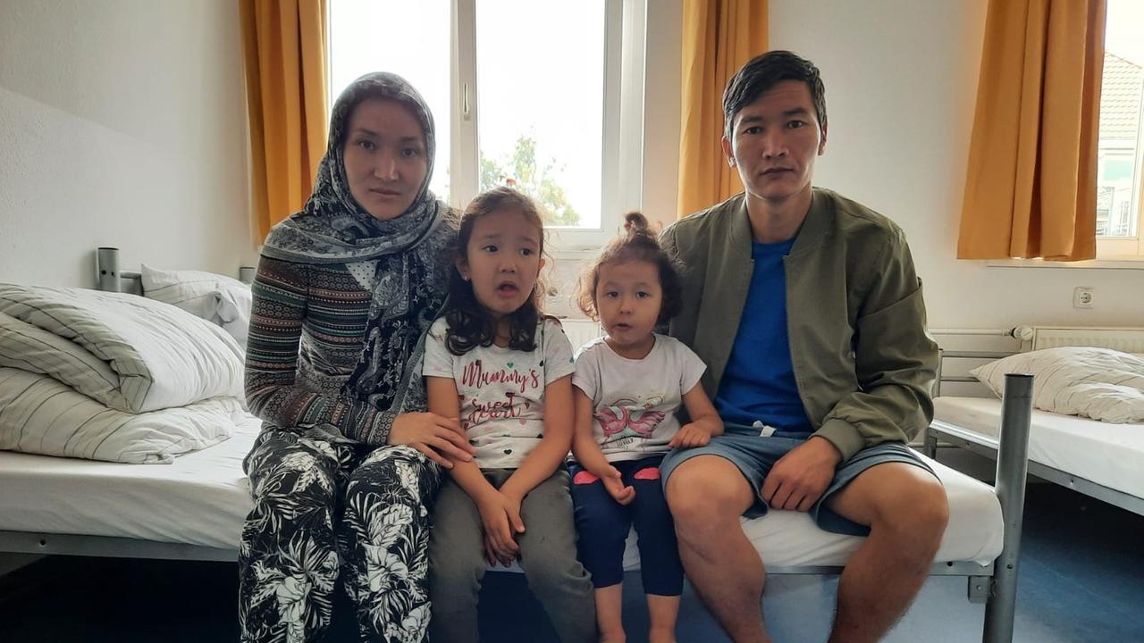 In einem Mehrbettzimmer eine Flüchtlingsunterkunft sitzen eine junge Frau und ein junger Mann mit ihren zwei kleinen Töchter auf der Kante eines Bettes. In einem Mehrbettzimmer eine Flüchtlingsunterkunft sitzen eine junge Frau und ein junger Mann mit ihren zwei kleinen Töchter auf der Kante eines Bettes.