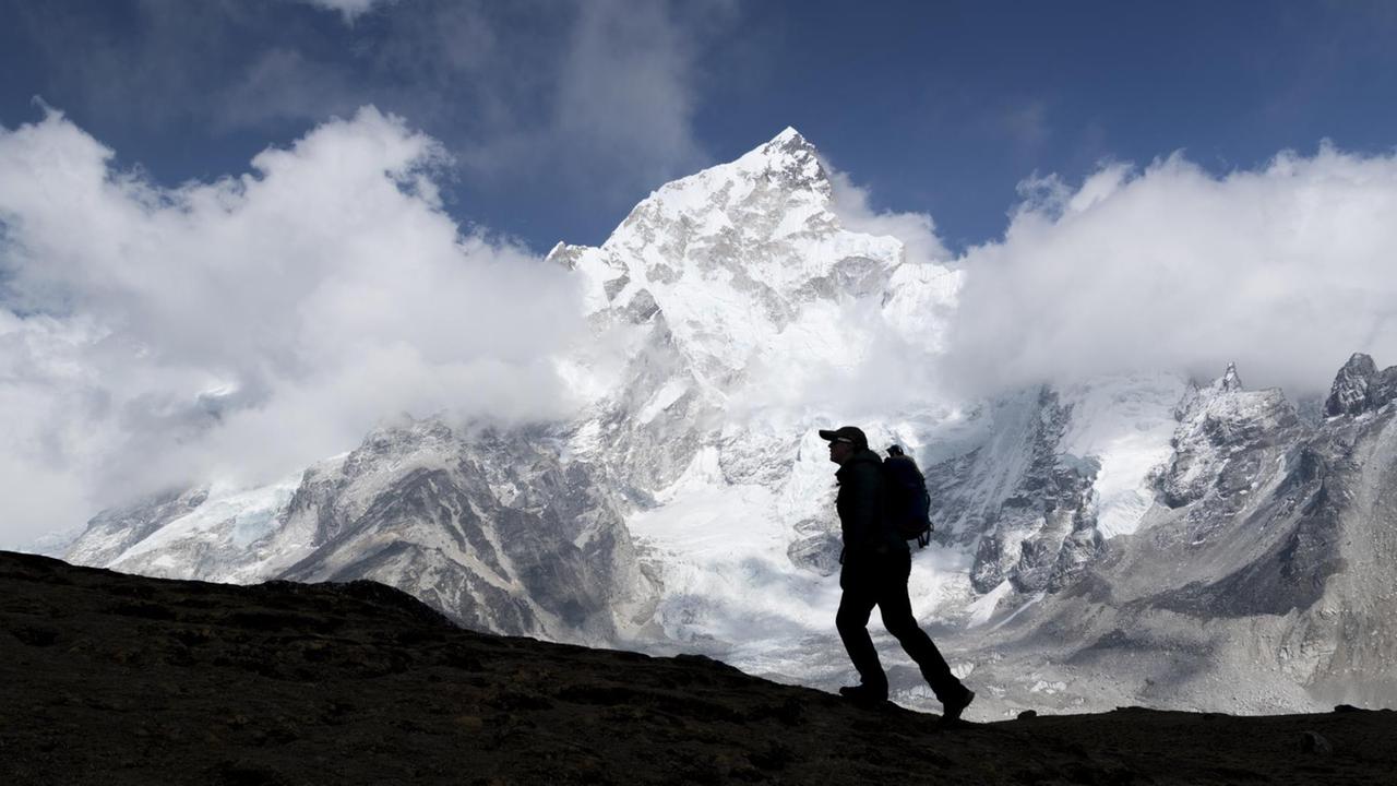 Im Vordergrund die Silhouette eines Bergsteigers, im Hintergrund der schneebedeckte Gipfel des Mount Everest Im Vordergrund die Silhouette eines Bergsteigers, im Hintergrund der schneebedeckte Gipfel des Mount Everest