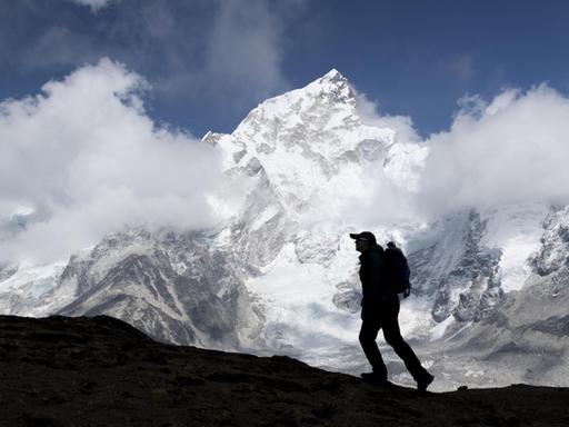 Im Vordergrund die Silhouette eines Bergsteigers, im Hintergrund der schneebedeckte Gipfel des Mount Everest