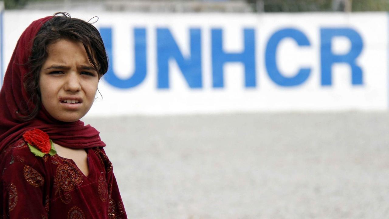 Ein Mädchen steht vor dem UNHCR-Logo in einem Flüchtlingscamp in Pakistan. Sie wartet auf ihre Ausbürgerung.