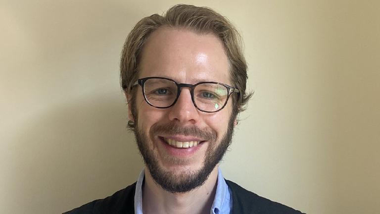 Ein lächelnder blonder Mann mit hoher Stirn, Brille und Backenbart in hellblauem Hemd und dunkelblauer Weste. Ein lächelnder blonder Mann mit hoher Stirn, Brille und Backenbart in hellblauem Hemd und dunkelblauer Weste.
