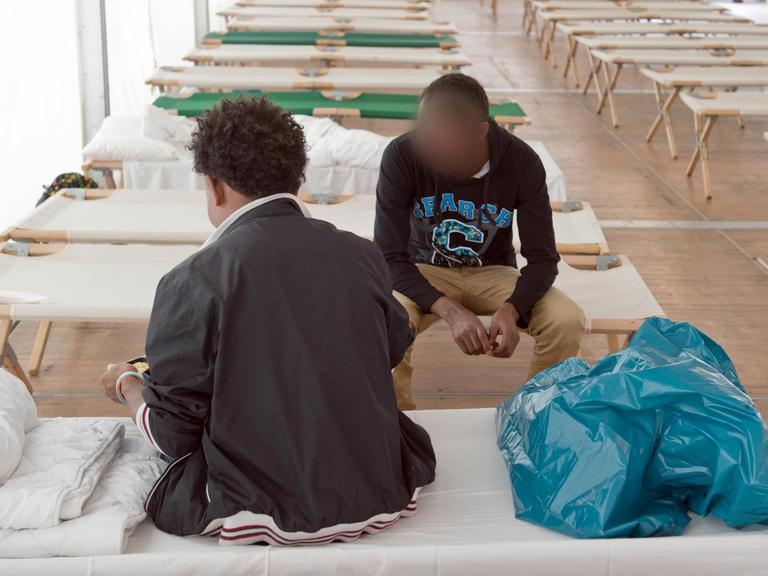 Aus Afrika stammende Flüchtlinge sitzen in einem Zelt einer Erstaufnahmeeinrichtung in Gießen.