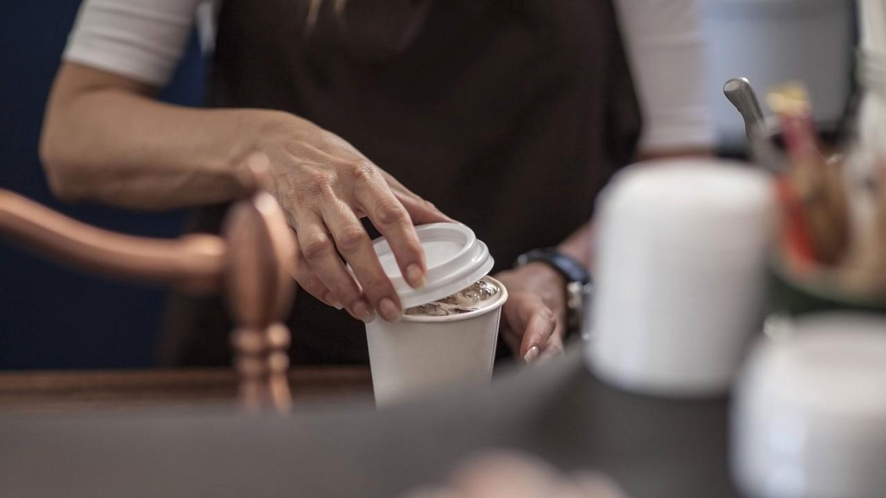 Ein Barista legt den Deckel auf einen Einweg-Kaffeebecher voller Kaffee. Ein Barista legt den Deckel auf einen Einweg-Kaffeebecher voller Kaffee.