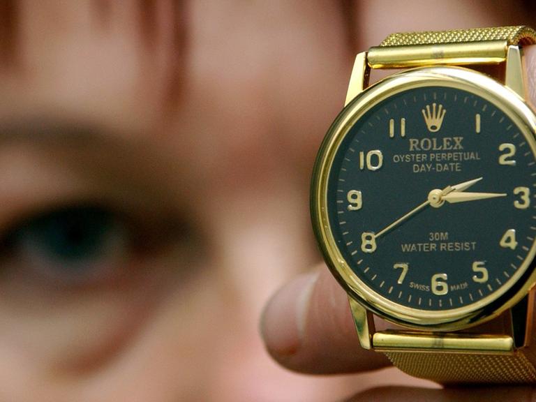 Eine Frau hält eine gefälschte Rolex-Uhr in die Kamera.