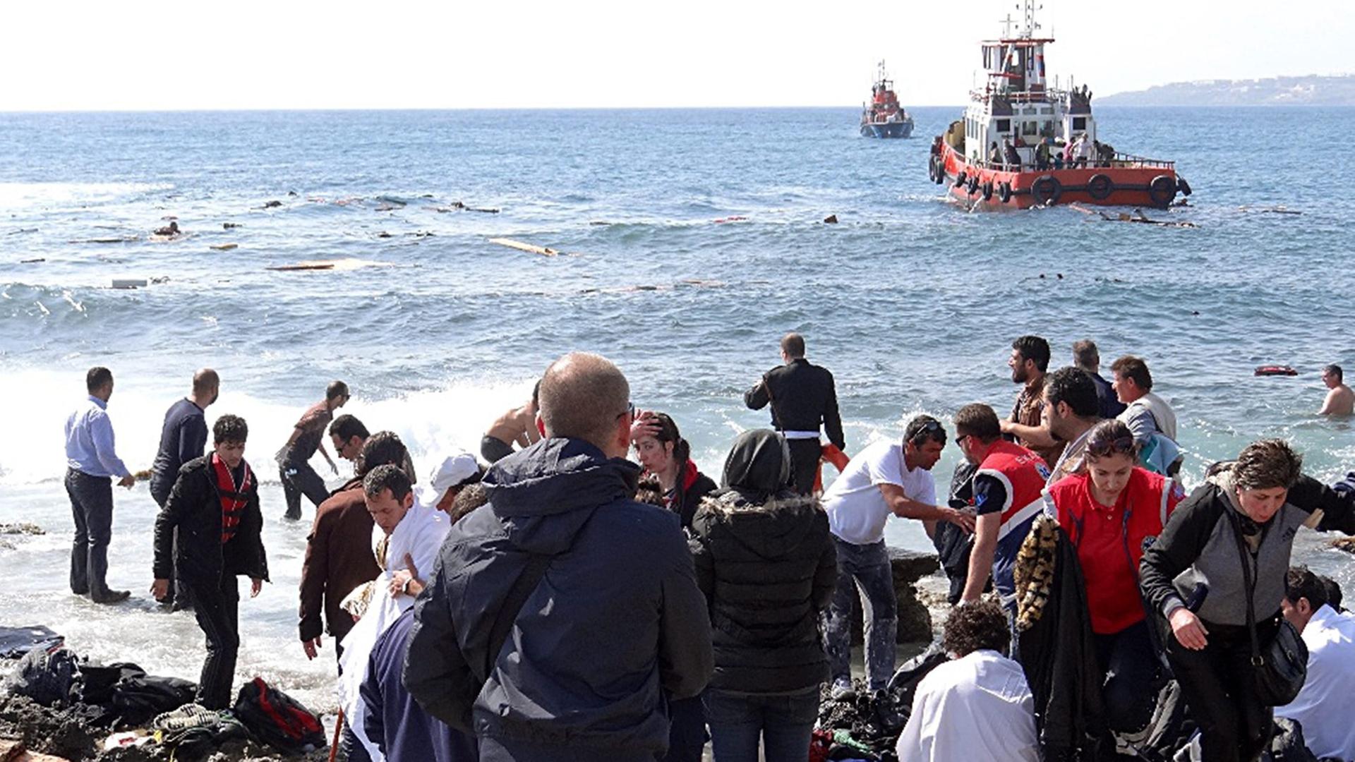 Zahlreiche Menschen stehen an einer Küste und beobachten ein auf Grund gelaufenes Schiff.
