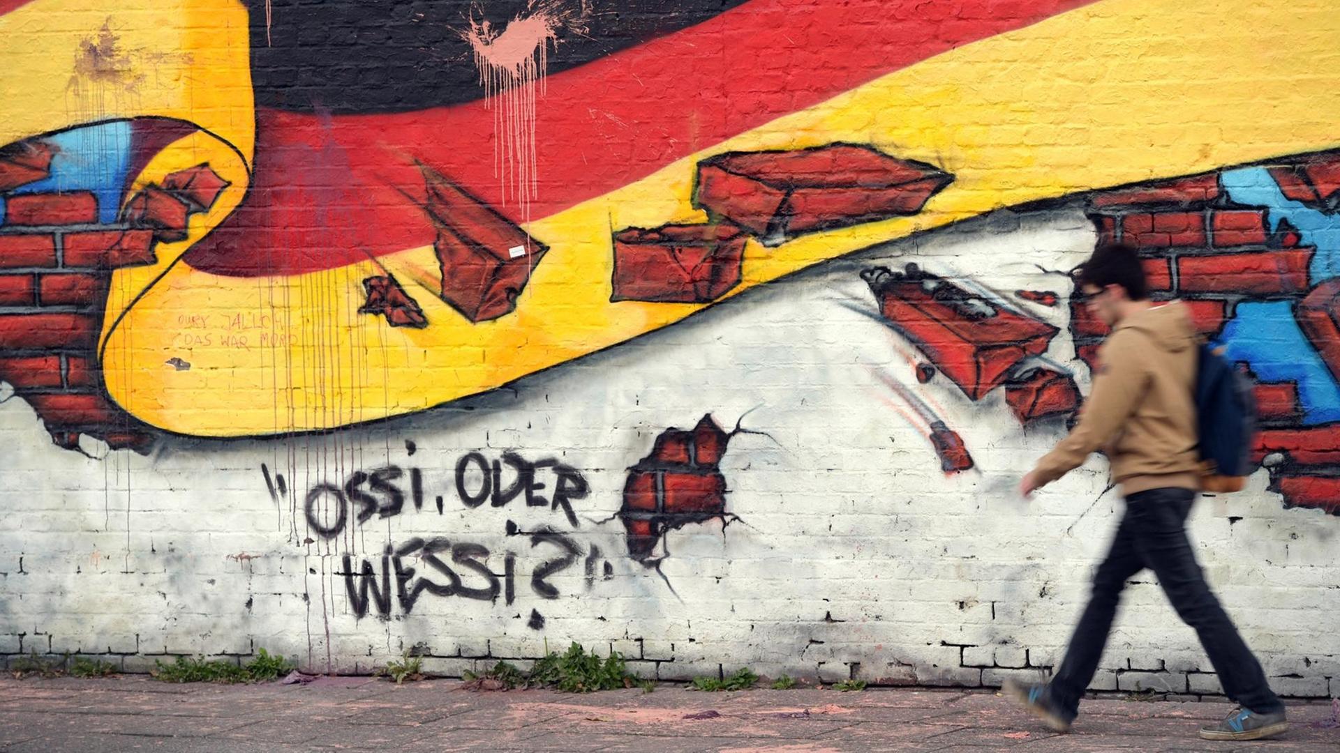 Ein Passant geht an einem Wandbild mit der deutschen Nationalflagge und dem Schriftzug "Ossi oder Wessi?" vorbei. Ein Passant geht an einem Wandbild mit der deutschen Nationalflagge und dem Schriftzug "Ossi oder Wessi?" vorbei.