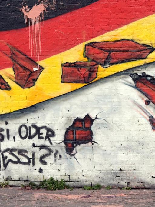 Ein Passant geht an einem Wandbild mit der deutschen Nationalflagge und dem Schriftzug "Ossi oder Wessi?" vorbei.