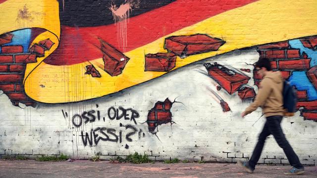 Ein Passant geht an einem Wandbild mit der deutschen Nationalflagge und dem Schriftzug "Ossi oder Wessi?" vorbei.