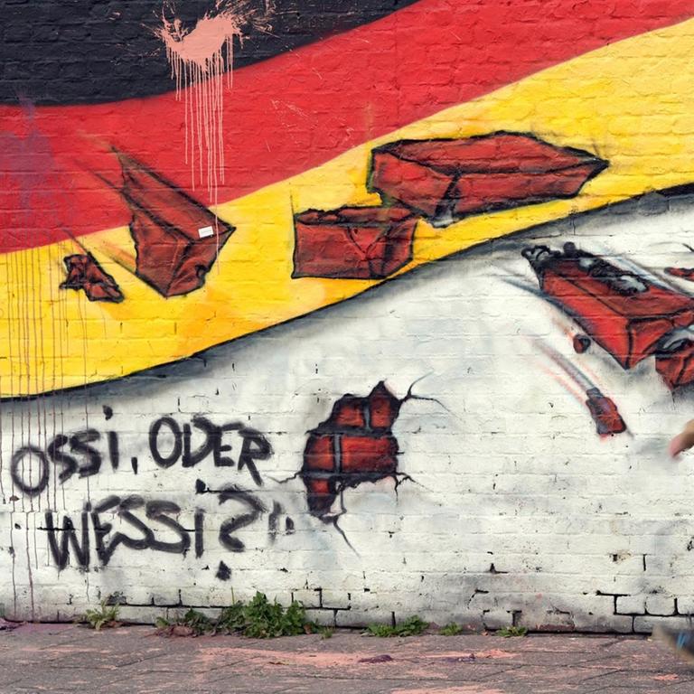 Ein Passant geht an einem Wandbild mit der deutschen Nationalflagge und dem Schriftzug "Ossi oder Wessi?" vorbei.