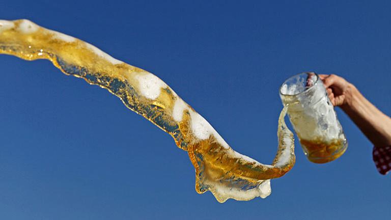 Bierglas wird ausgeleert, Bier fliegt durch die Luft Bierglas wird ausgeleert, Bier fliegt durch die Luft