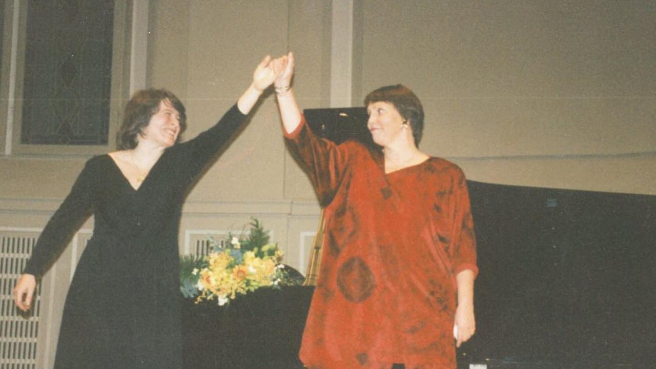 Undatiertes Foto der Pianistin und der Sängerin in einem großen roten Gewand, die gemeinsam ihre Hände kurz vor einer Verbeugung in die Luft heben. Undatiertes Foto der Pianistin und der Sängerin in einem großen roten Gewand, die gemeinsam ihre Hände kurz vor einer Verbeugung in die Luft heben.