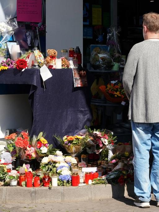 Blumen, Kerzen und Botschaften an das Opfer liegen vor der Tankstelle, an der ein Maskengegner einen Angestellten erschossen hat. Zwei Menschen stehen vor den Blumen.