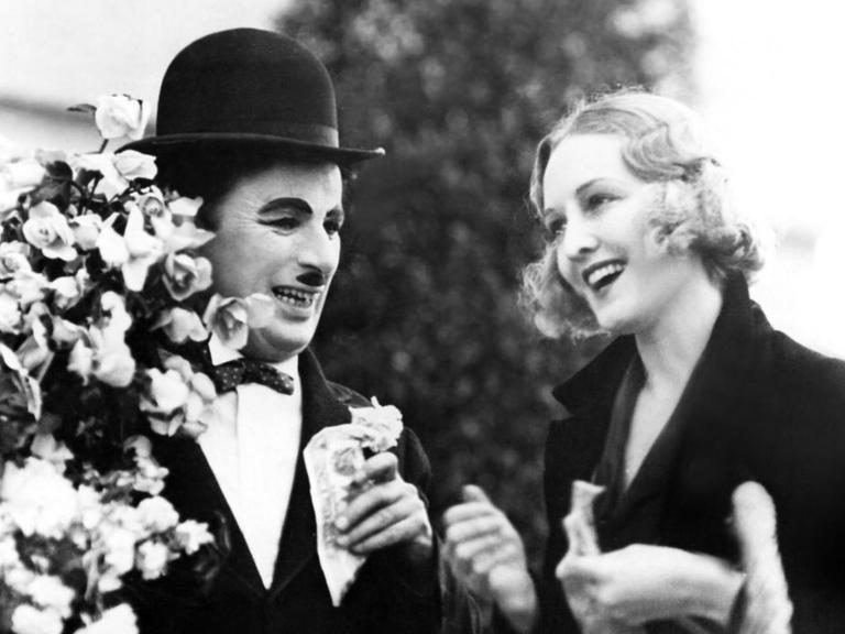 Ein schwarzweißer Filmausschnitt zeigt Charlie Chaplin als Tramp und Virginia Cherrill als blindes Blumenmädchen in "Lichter der Großstadt" von 1931