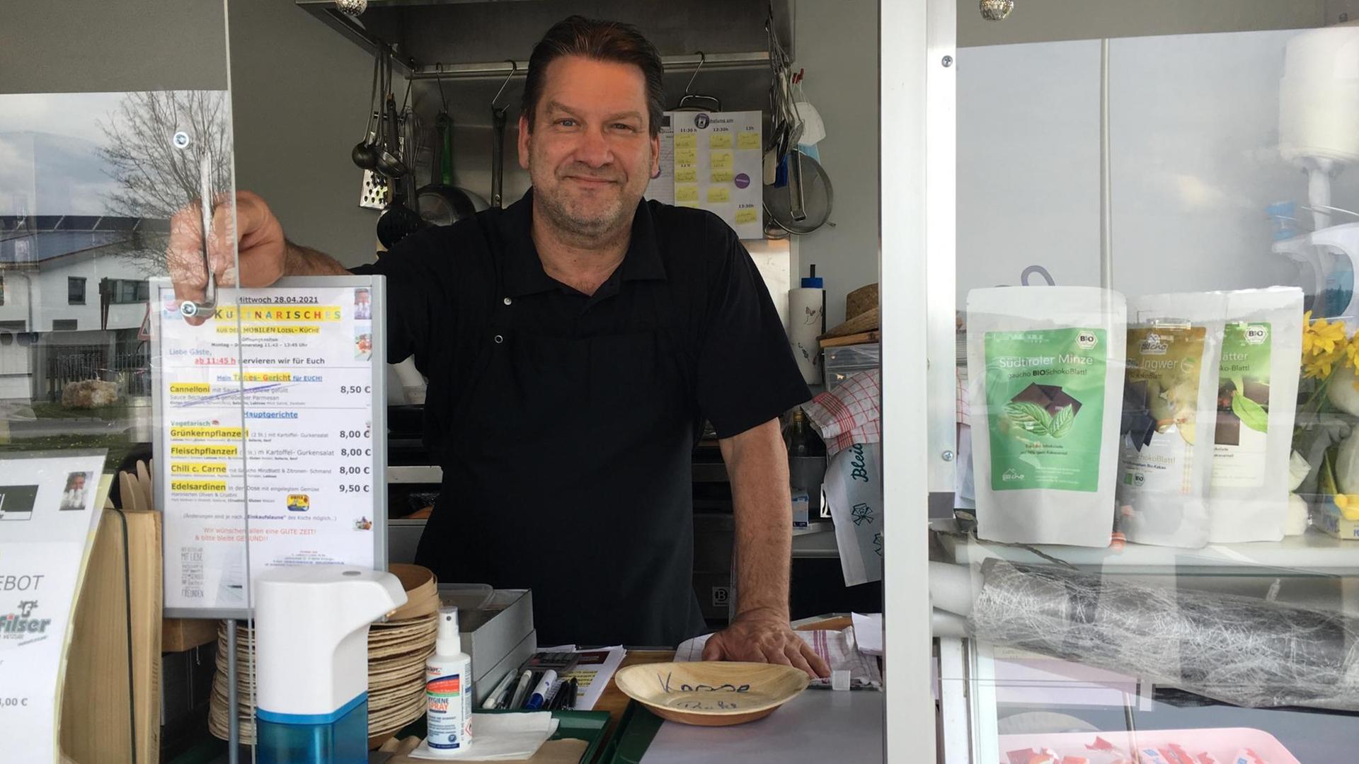 Christian Loisl in der Bildmitte blickt aus seiner Imbissbude, links ist die Karte zu sehen, rechts einige Waren zum Verkauf, etwa Bio-Milch und Schokolade. Christian Loisl in der Bildmitte blickt aus seiner Imbissbude, links ist die Karte zu sehen, rechts einige Waren zum Verkauf, etwa Bio-Milch und Schokolade.