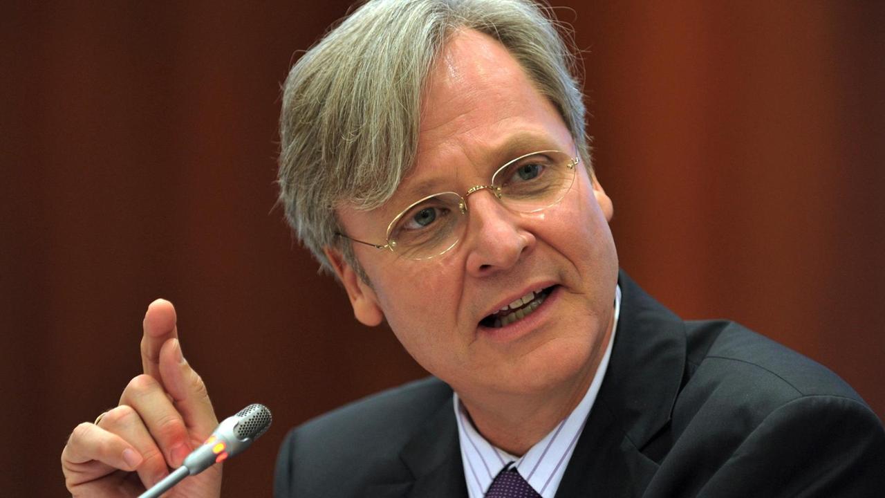 Wansleben spricht vor einem braunen Hintergrund gestikulierend in ein Mikrofon. Wansleben spricht vor einem braunen Hintergrund gestikulierend in ein Mikrofon.