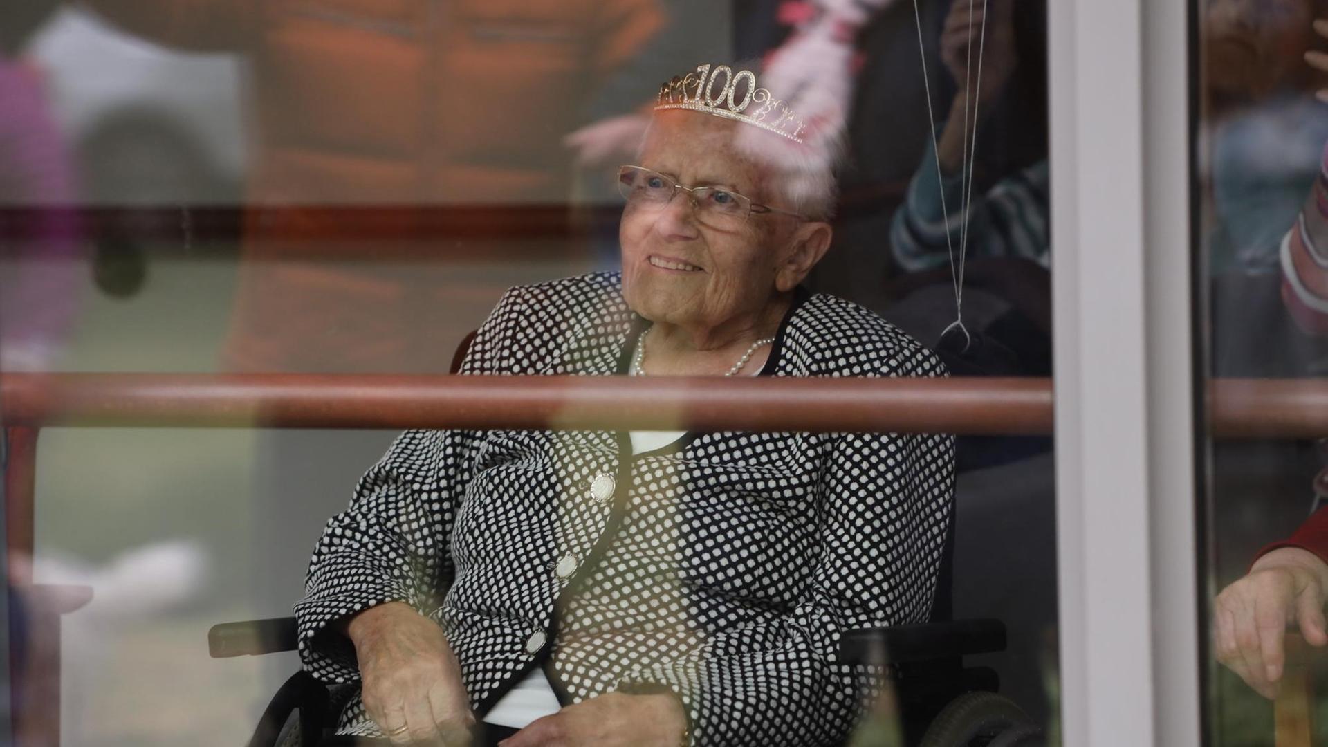 Agnes Senker sitzt hinter einer Scheibe und trägt eine Krone mit der Zahl 100.