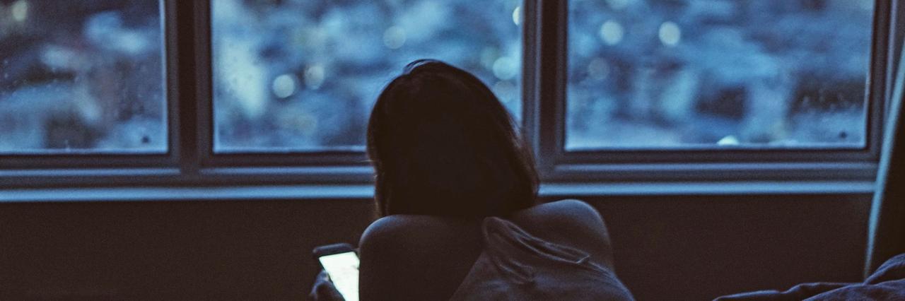 Eine junge Frau liegt bäuchlings im Bett und schaut auf ihr Smartphone. Eine junge Frau liegt bäuchlings im Bett und schaut auf ihr Smartphone.