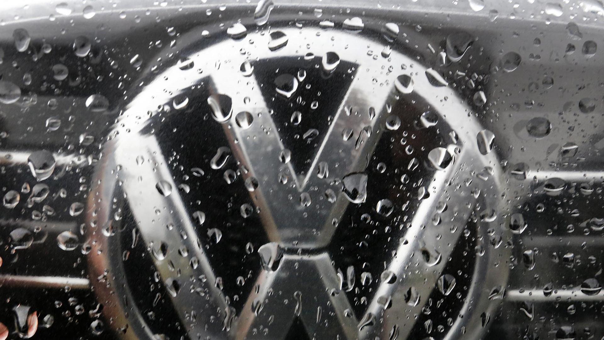 Das Bild zeigt ein VW-Logo auf einem Auto. Es ist voller Regentropfen.