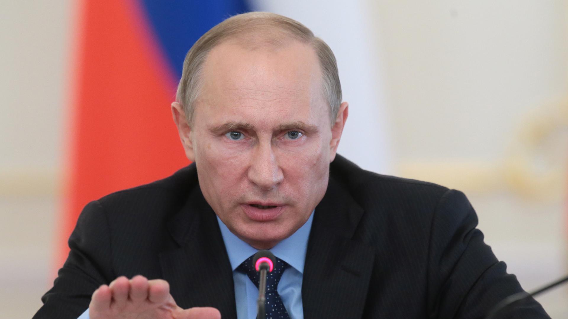 Wladimir Putin sitzt an einem Mikrofon, gestikuliert und spricht Wladimir Putin sitzt an einem Mikrofon, gestikuliert und spricht