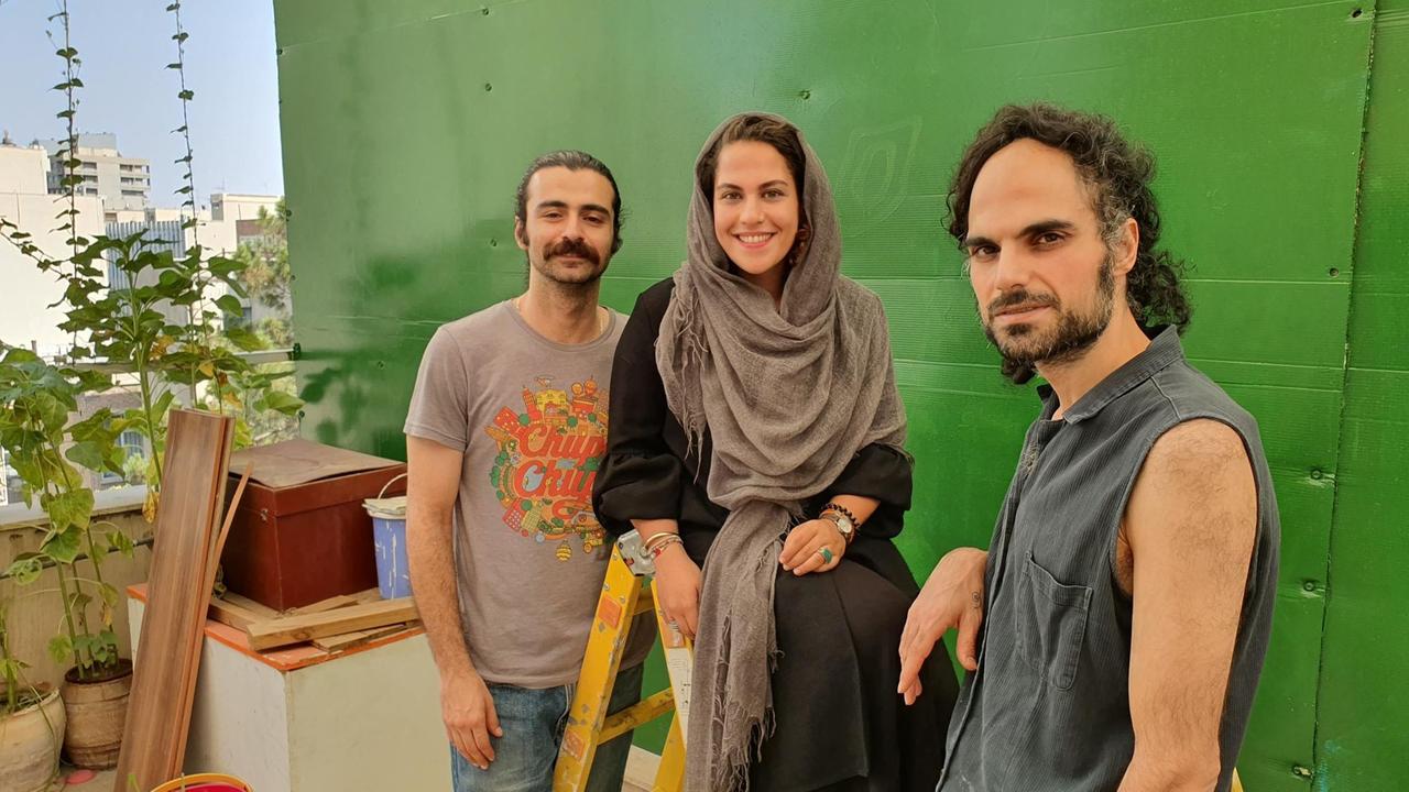 Mohammadreza Hariri,  Shadi Tabibzadeh,, Siyavash Sohi stehen auf der Terrasse vor eine grünen Wand und lächeln in die Kamera.