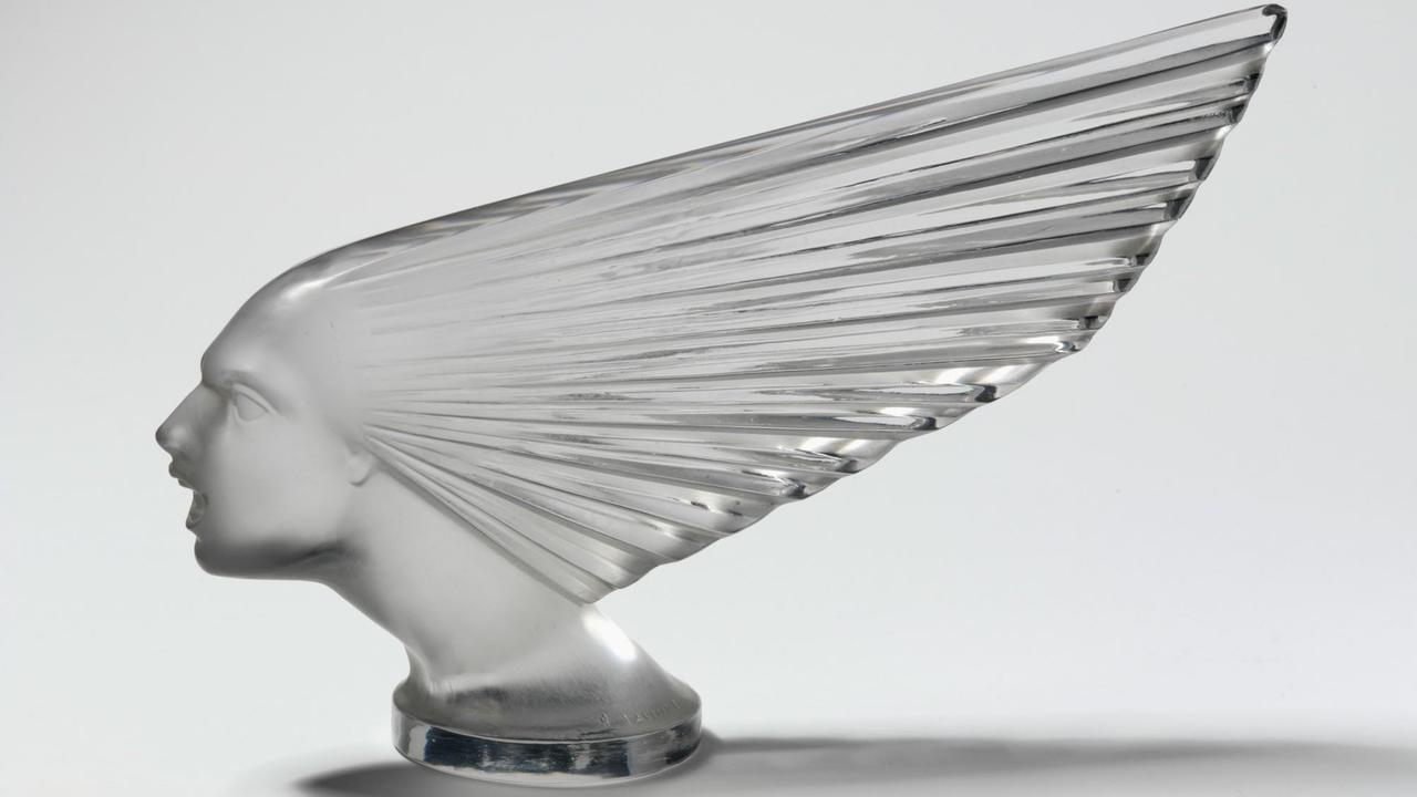 Eine durchsichtige Kühlerfigur aus Glas, hier: ein nach vorne gestreckter Kopf mit einem Windschweif, der die Haare symbolisieren soll.