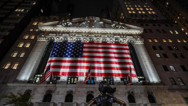 Die Börse an der New Yorker Wall Street ist mit der US-Flagge geschmückt, die von Scheinwerfern angeleuchtet werden.