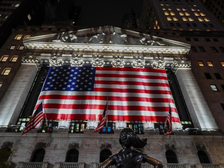 Die Börse an der New Yorker Wall Street ist mit der US-Flagge geschmückt, die von Scheinwerfern angeleuchtet werden.