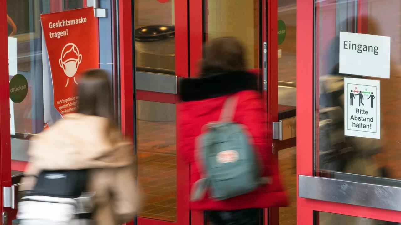 Schüler und Schülerinnen der Städtischen Integrierten Gesamtschule Paffrath gehen durch den Eingang der Schule, an dessen Scheiben Hinweiszettel kleben, die auf die Maskenpflicht und die Abstandsregeln hinweisen. Schüler und Schülerinnen der Städtischen Integrierten Gesamtschule Paffrath gehen durch den Eingang der Schule, an dessen Scheiben Hinweiszettel kleben, die auf die Maskenpflicht und die Abstandsregeln hinweisen.