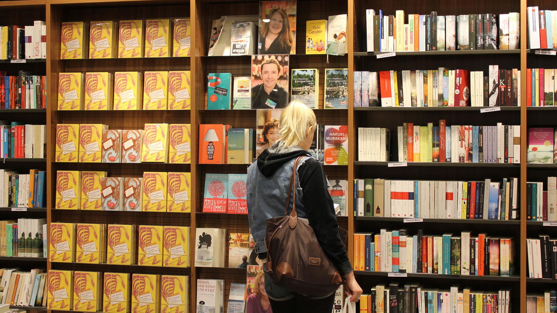 Eine junge Frau steht unschlüssig vor Bücherregalen in einer Buchhandlung Eine junge Frau steht unschlüssig vor Bücherregalen in einer Buchhandlung