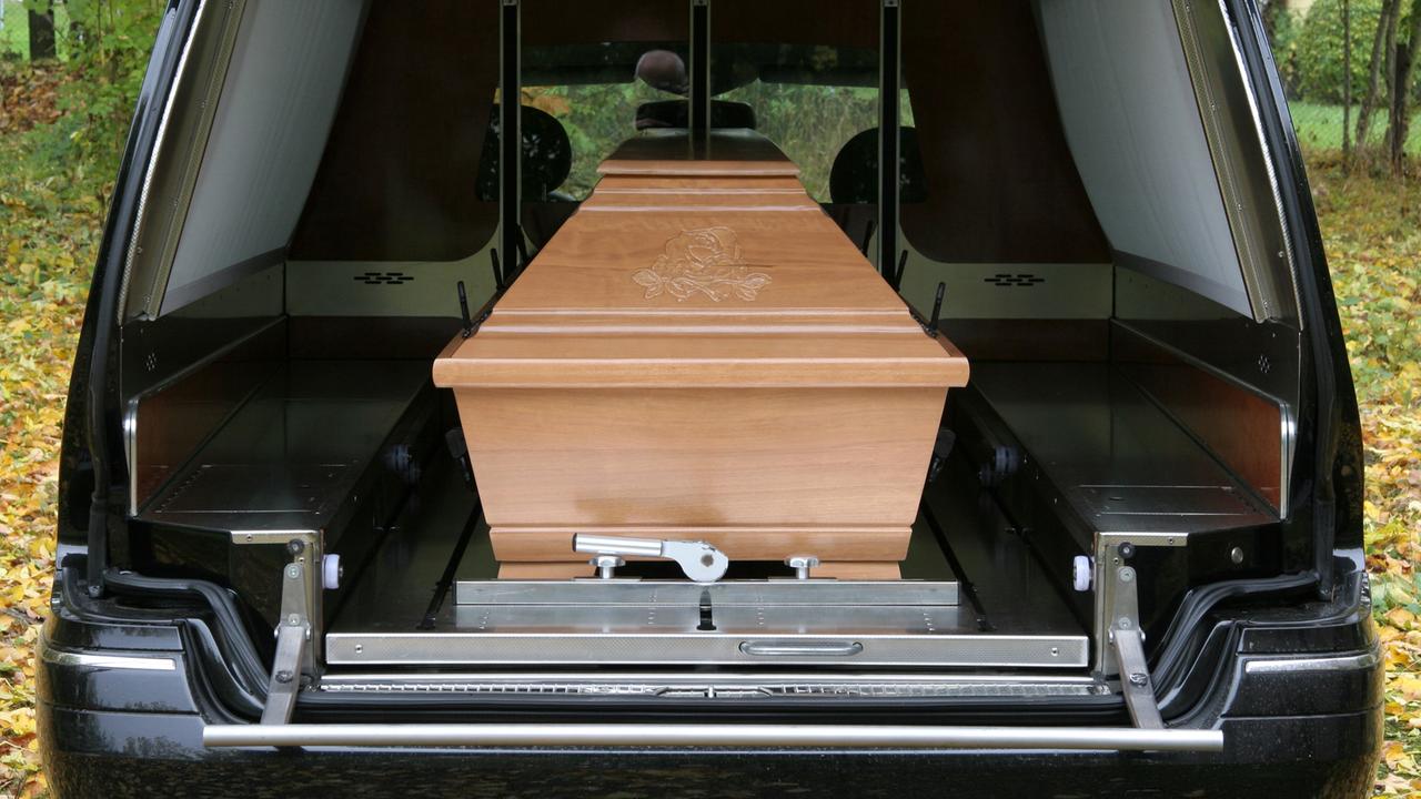 Ein Holzsarg in einem Auto eines Bestattungsunternehmens bei einer Beerdigung Ein Holzsarg in einem Auto eines Bestattungsunternehmens bei einer Beerdigung