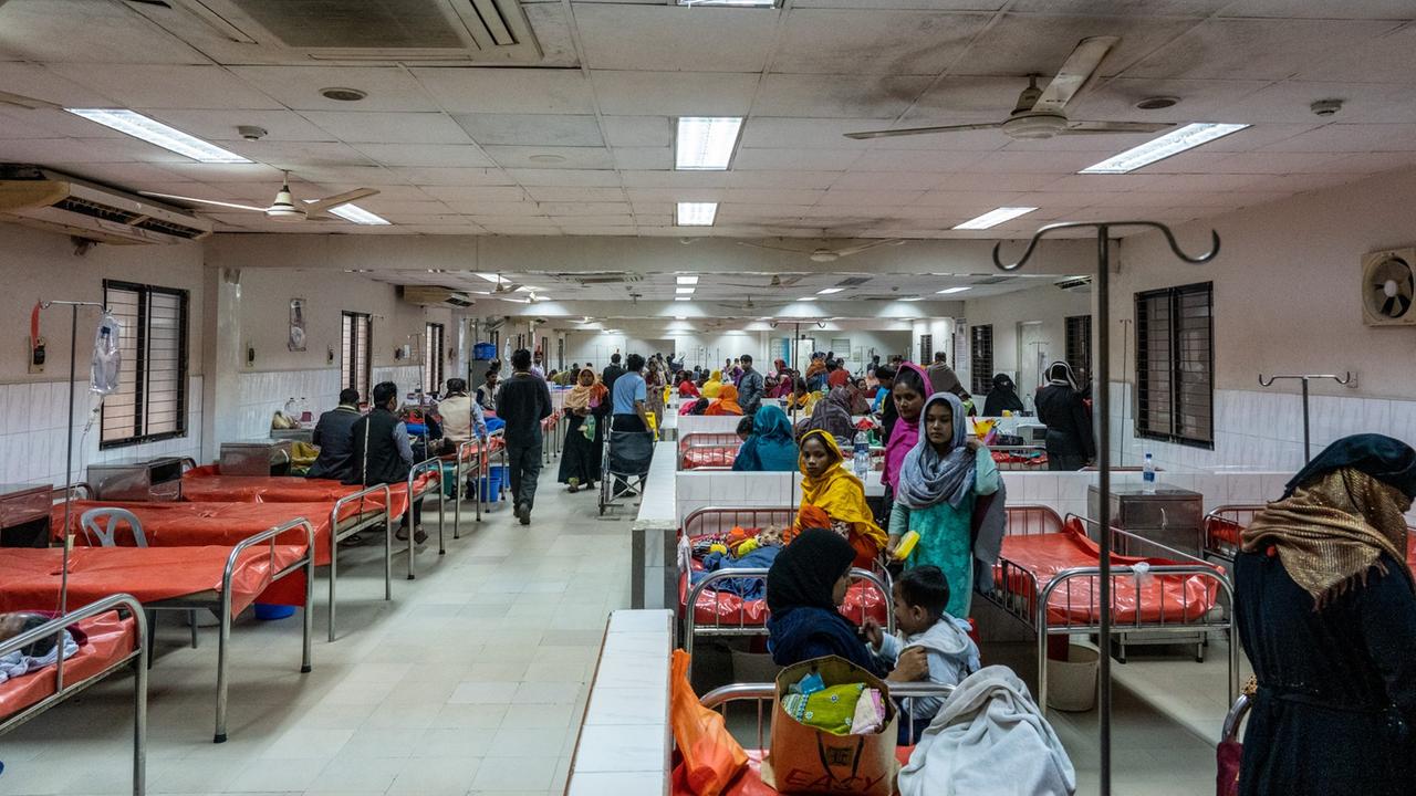In einem Krankensaal im Cholerakrankenhaus, International Centre for Diarrhoeal Disease Research, Bangladesh (icddr,b) in Dhaka stehen dicht nebeneinander Betten mit Metallrahmen und rotem Gummibezügen mit einem Loch in der Mitte. An den belegten Betten stehen Angehörige der Patienten. In einem Krankensaal im Cholerakrankenhaus, International Centre for Diarrhoeal Disease Research, Bangladesh (icddr,b) in Dhaka stehen dicht nebeneinander Betten mit Metallrahmen und rotem Gummibezügen mit einem Loch in der Mitte. An den belegten Betten stehen Angehörige der Patienten.