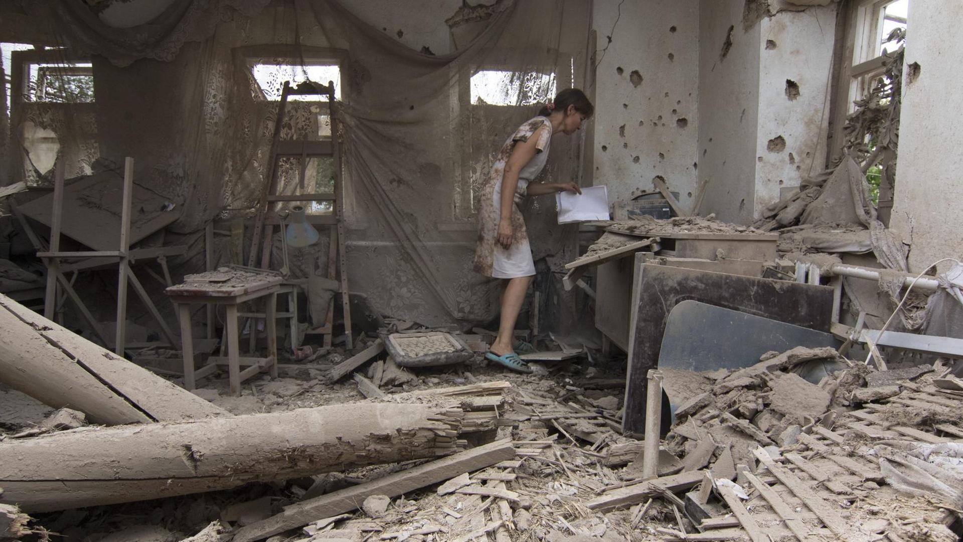 Eine Frau steht in einem völlig zerstörten Haus in dem Dorf Sartan nahe Mariupol