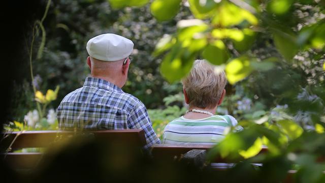 Ein älteres Paar sitzt in einem Park auf einer Bank im Sonnenschein.