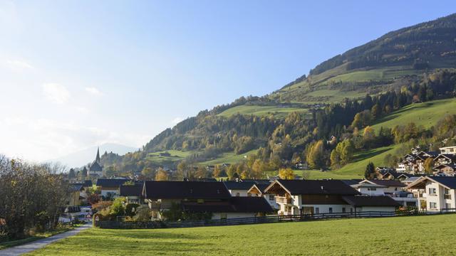 Blick auf das Dorf Stuhlfelden im Salzburger Land in Österreich: Hinter dem Dorf sind Berge und darüber blauer Himmel zu sehen.