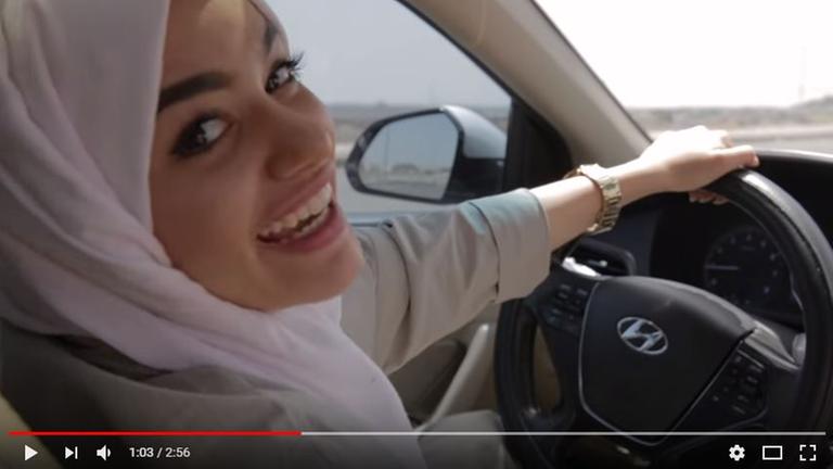 Videostill von Leesa A., der ersten rappenden Autofahrerin im islamischen Königreich, sie sitzt am Steuer und lacht in die Kamera