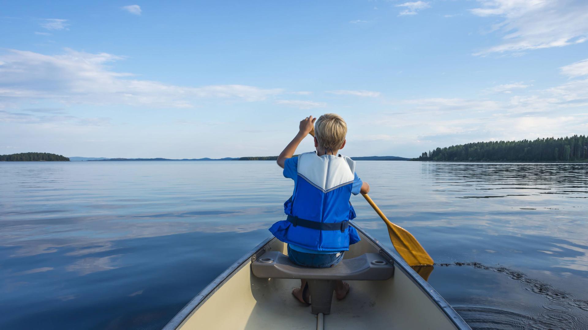 Aufnahme eines paddelnden Kindes von hinten mit Blick auf den weiten See. Aufnahme eines paddelnden Kindes von hinten mit Blick auf den weiten See.