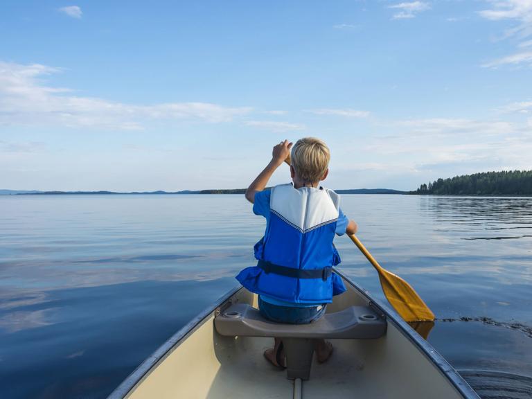 Aufnahme eines paddelnden Kindes von hinten mit Blick auf den weiten See.