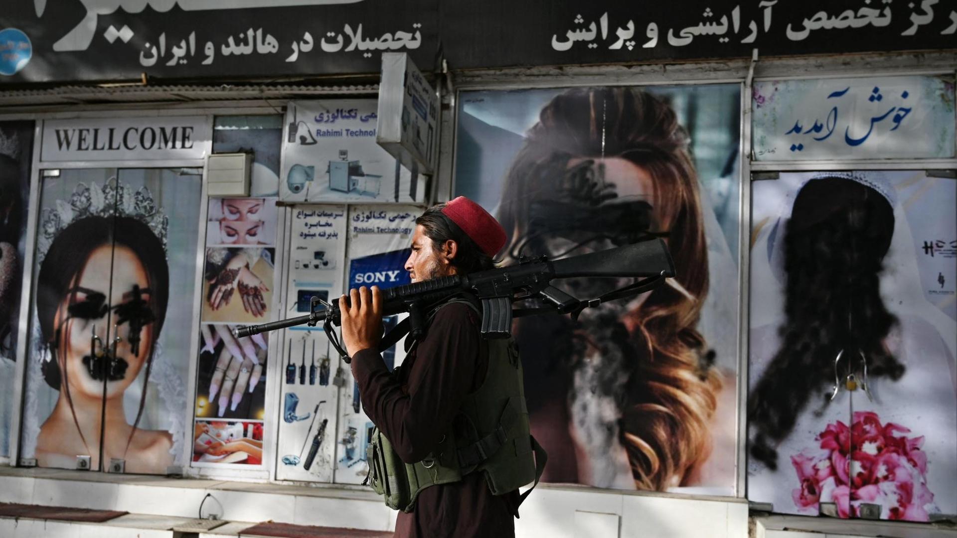 Ein Taliban-Kämpfer geht am 18. August 2021 in Shar-e-Naw in Kabul an einem Schönheitssalon vorbei, in dem Bilder von Frauen mit Sprühfarbe verunstaltet wurden. Ein Taliban-Kämpfer geht am 18. August 2021 in Shar-e-Naw in Kabul an einem Schönheitssalon vorbei, in dem Bilder von Frauen mit Sprühfarbe verunstaltet wurden.