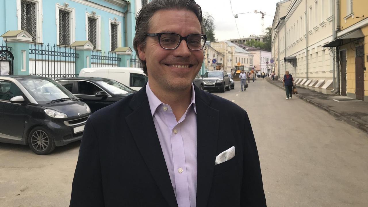 Lächelnder Mann auf einer Straße, im Hintergrund parkende Autos Lächelnder Mann auf einer Straße, im Hintergrund parkende Autos