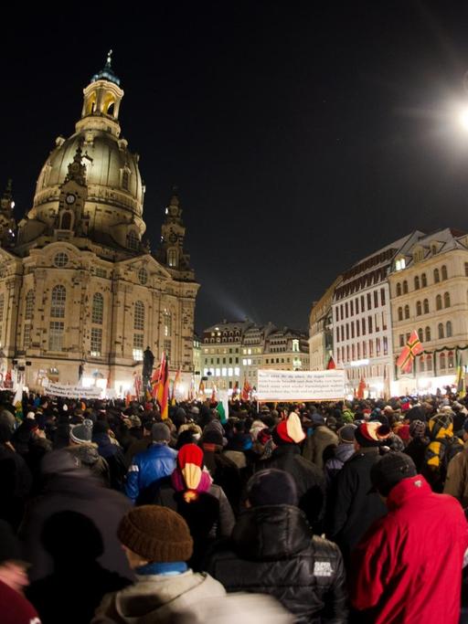 Menschenmenge mit Deutschlandfahnen vor der Dresdner Frauenkirche bei Dunkelheit.