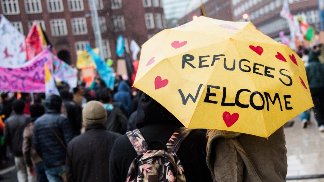 Eine Frau und ein Mann mit einem Regenschirm mit der Aufschrift "Refugees welcome" nehmen in der Innenstadt in Hamburg an einer Demonstration für die Rechte von Flüchtlingen teil.