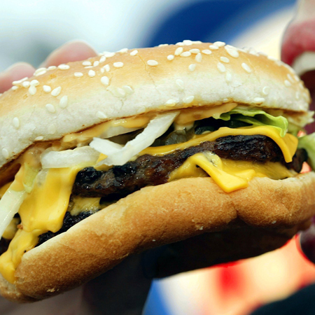 Ein Mund ist weit geöffnet, um in einen Cheeseburger zu beißen. Ein Mund ist weit geöffnet, um in einen Cheeseburger zu beißen.