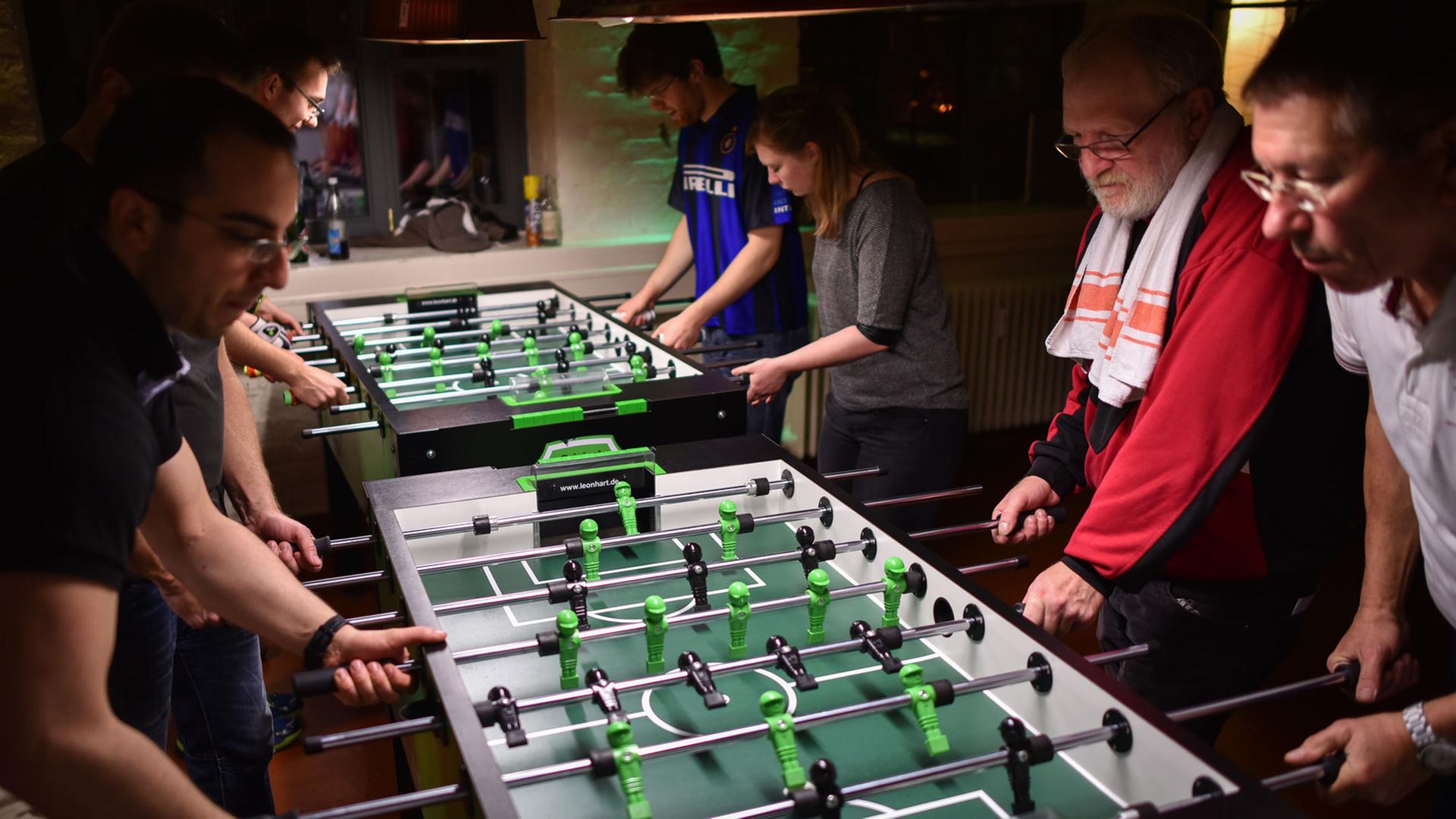 Tischfußballer spielen konzentriert an Kickertischen. Einer hat ein Handtuch über den Schultern hängen. Tischfußballer spielen konzentriert an Kickertischen. Einer hat ein Handtuch über den Schultern hängen.