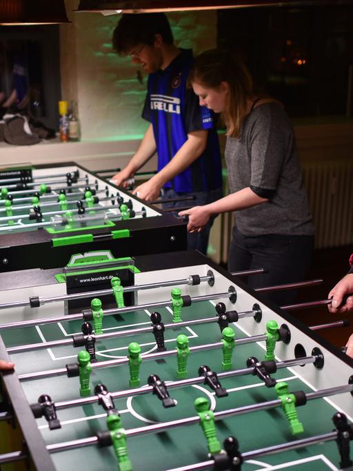 Tischfußballer spielen konzentriert an Kickertischen. Einer hat ein Handtuch über den Schultern hängen.